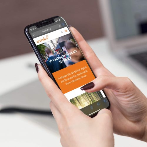 Händer som håller i en mobiltelefon och på skärmen visas hemsida från kundprojekt