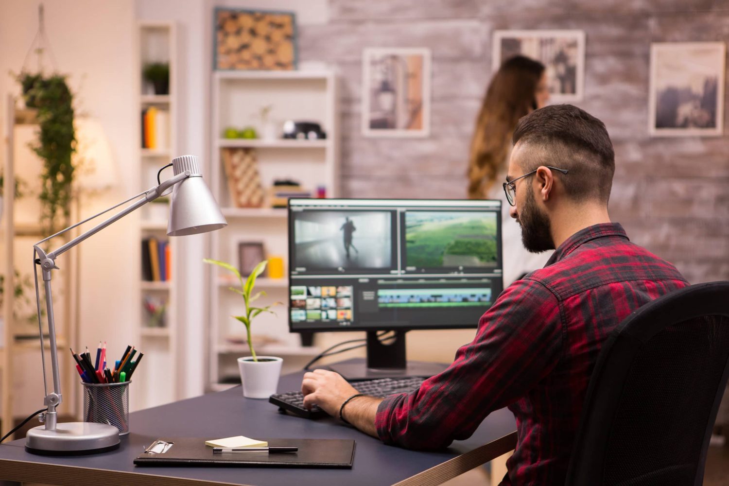 En man sedd bakifrån sitter och arbetar med videoredigering på dator i kontorsmiljö