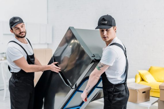 Två flyttarbetare bär ett kylskåp i rostfritt stål