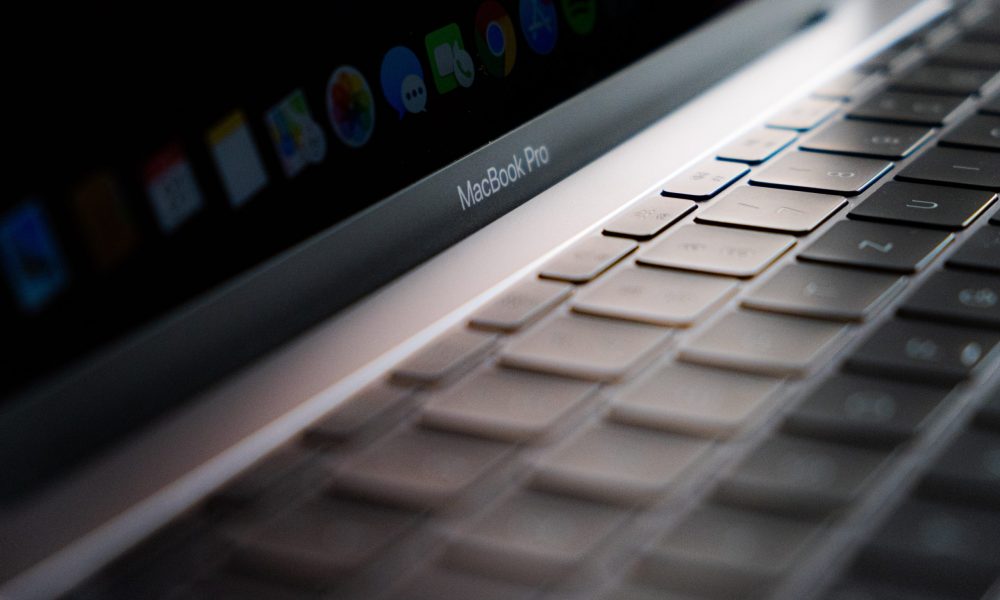 Närbild på tangentbord med svarta tangenter på en bärbar dator i silverfärg. Märket som syns är Macbook Pro